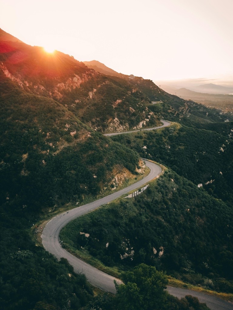 A winding mountain road at sunset disappearing into the hills, symbolizing steady progress through a step-by-step process