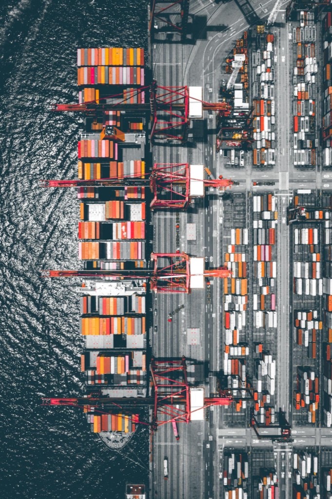 Aerial view of a shipping port with container ship, gantry cranes, and stacked containers representing international trade and customs clearance