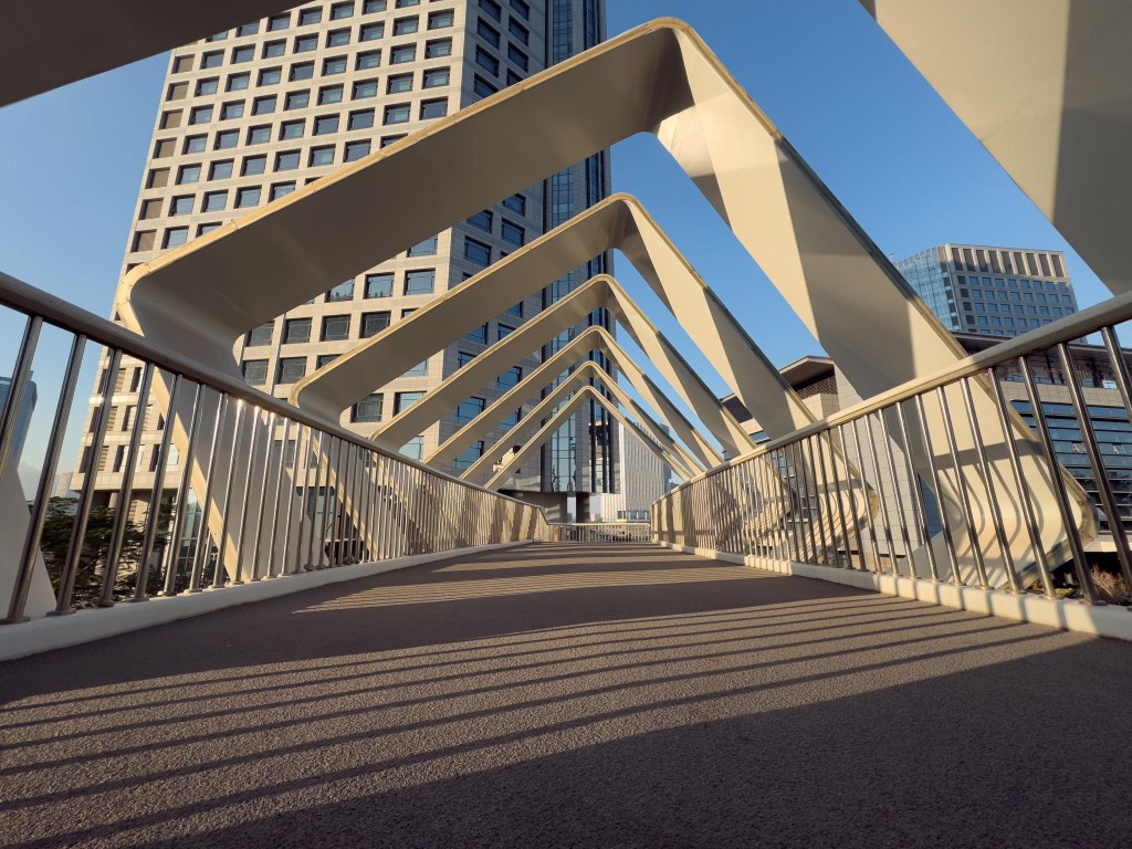 A modern pedestrian bridge with repeating white arches receding into the distance, suggesting consistency and forward movement