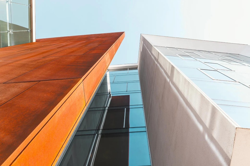 Modern building facades in rust-orange steel and reflective glass converging upward, symbolizing two perspectives on the same business